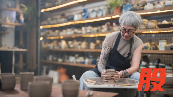 陶艺工作室里，一位老年女性匠人在陶轮上制作陶碗